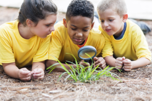 three young kids using a magnifying glass